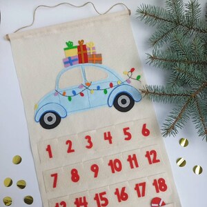 May include: A felt Christmas advent calendar with a light blue car carrying gifts and a string of lights. The calendar has 24 numbered pockets in red, with a small candy cane in pocket 24. A festive holiday decoration.