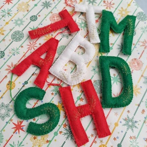 Può includere: Addobbi natalizi in feltro a forma delle lettere "SHADTM", con ricamo dorato. Le lettere sono rosse e verdi.