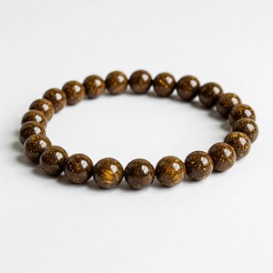 Puede incluir: Un brazalete de cuentas marrones con motas doradas. Las cuentas son redondas y lisas.