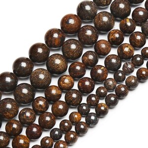 Puede incluir: Primer plano de hilos de cuentas de piedras preciosas marrones. Las cuentas son redondas con un aspecto pulido y moteado. El color varía del marrón oscuro a tonos más claros, creando una estética natural y terrosa. Las cuentas son de diferentes tamaños.