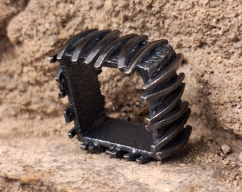 May include: A silver ring with a square design. The ring is made of metal and has a textured surface.