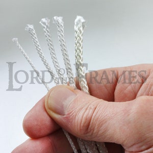May include: Five different sizes of white braided cord, held in a hand. The cord is commonly used for hanging pictures.