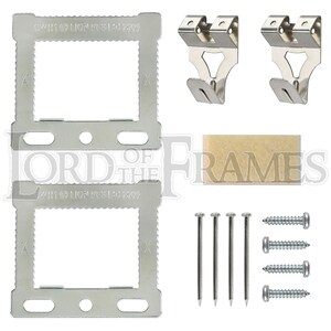May include: Two silver metal picture hanging frames with a small piece of brown felt, two silver metal hooks, and six silver screws and nails. The frames have the text "WH11 LIOA PES LA1 2203" printed on them.