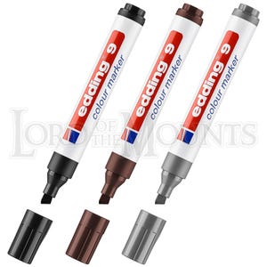 May include: Three Edding 9 colour markers in black, brown, and grey, with their caps off and lying below. The markers have a white barrel with red and blue accents and the text "edding 9 colour marker".