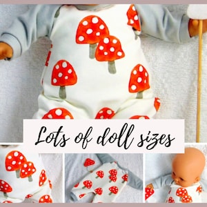 Pode incluir: Um macacão branco com estampa de cogumelos vermelhos e brancos. O macacão tem mangas cinzas e está disponível em vários tamanhos para bonecas. O texto "Lots of doll sizes" está escrito na imagem.