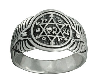 May include: A silver ring with a detailed design featuring a six-pointed star with Hebrew lettering inside a circle, flanked by two stylized wings.