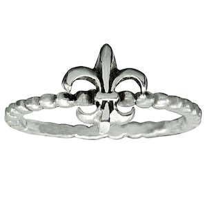 Puede incluir: Un anillo de plata con un diseño de flor de lis. La banda es texturizada y la flor de lis está en relieve.