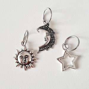 May include: Three silver-toned charms: a sun with a face, a crescent moon with a face, and a star. Each charm has a small ring attached for hanging. The charms are on a white background.