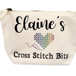 May include: Cream-colored canvas pouch with a zipper closure. The pouch features the name "Elaine's" in black script above a cross-stitch heart in rainbow colors. Below the heart, the text "Cross Stitch Bits" is printed.