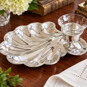 May include: A polished silver-toned serving tray shaped like a large scallop shell, featuring a matching silver-toned pedestal base that holds a removable clear glass bowl insert, creating a cohesive two-piece serving set.