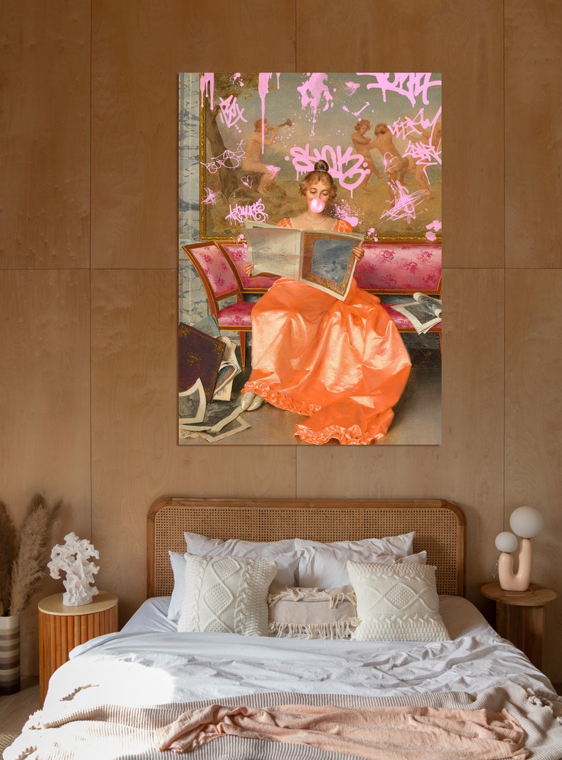 May include: A woman in a long orange dress sits on a pink and gold couch, reading a book. The background is a painting with pink graffiti.