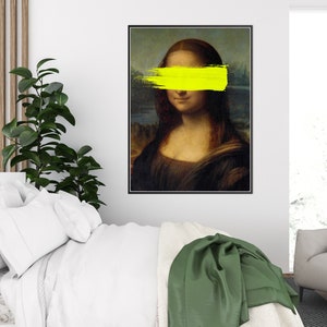 May include: A framed print of the Mona Lisa painting with a yellow paint stroke covering her eyes.