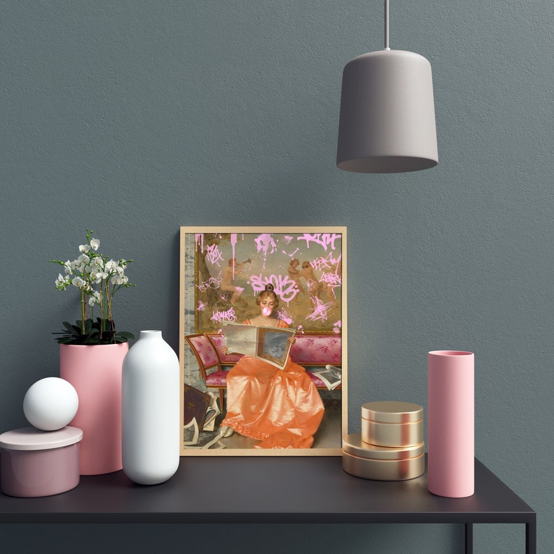 May include: A framed print of a woman in a vintage dress reading a book. The woman is wearing a pink bubble and the background is covered in pink graffiti.