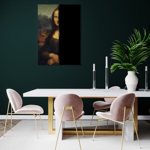 May include: A framed print of the Mona Lisa, bisected by a black vertical line. The artwork is displayed above a white table with gold legs, complemented by pink velvet chairs with gold frames. A white vase with greenery and candles decorates the dining area.