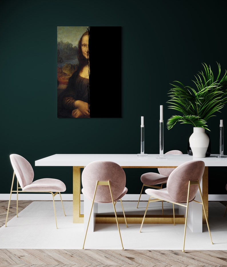 May include: A framed print of the Mona Lisa, bisected by a black vertical line. The artwork is displayed above a white table with gold legs, complemented by pink velvet chairs with gold frames. A white vase with greenery and candles decorates the dining area.