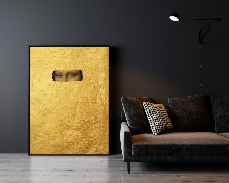 May include: A framed artwork featuring a textured gold background with a rectangular cutout revealing the eyes of the Mona Lisa. The artwork is displayed against a dark wall, next to a dark gray sofa with a patterned pillow.