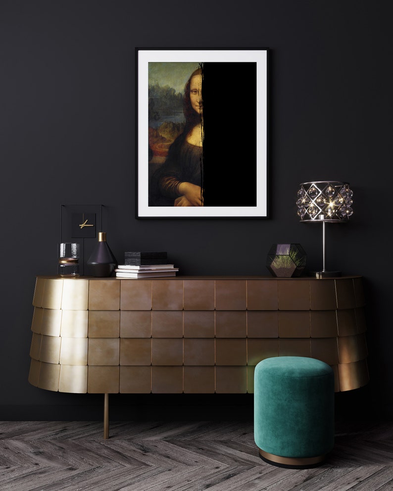 May include: A framed print of the Mona Lisa, partially obscured by a black vertical stripe, hangs above a gold-toned cabinet. A green velvet stool and a crystal lamp add to the room's decor. The room has dark walls and a wooden floor.