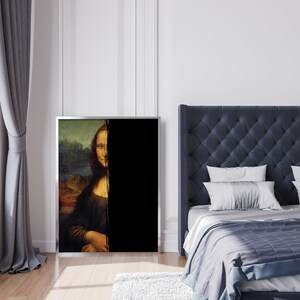 May include: A framed print of the Mona Lisa painting, with a vertical black stripe obscuring half the image. The artwork is in a silver frame and leans against a white wall. The room has a bed with a blue headboard.