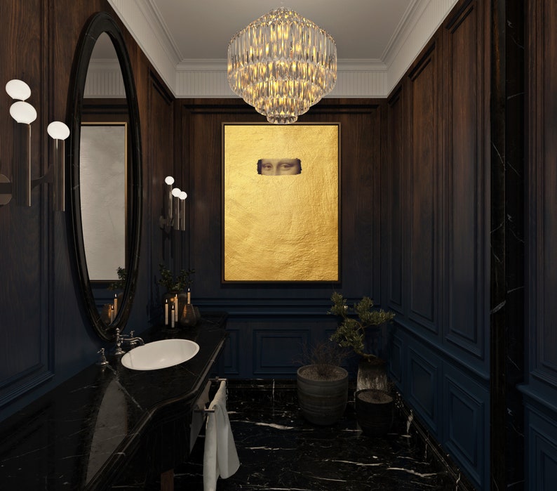 May include: A luxurious bathroom with dark wood paneling and a black marble countertop. A large gold artwork with eyes is centered on the wall. A crystal chandelier hangs from the ceiling, and an oval mirror is on the wall.