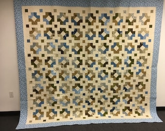 May include: A large quilt with a geometric pattern in shades of blue, brown, and white. The quilt is made up of squares and rectangles, and the pattern is repeated throughout the quilt.
