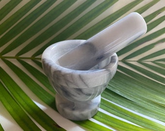 May include: A white marble mortar and pestle with gray veining. The mortar and pestle are sitting on a green and white striped surface.
