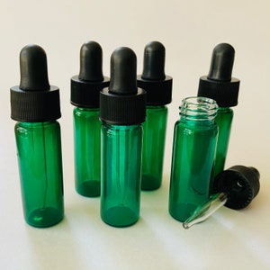 May include: Six green glass bottles with black dropper tops. The bottles are all the same size and shape. One bottle is lying on its side with the dropper removed.