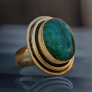 Puede incluir: Un anillo de oro con una gran piedra preciosa verde de forma ovalada engastada en un bisel de doble capa.