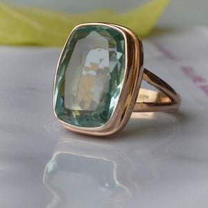 Puede incluir: Un anillo con una gran piedra rectangular de color azul claro engastada en una banda de oro.