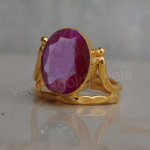 Könnte beinhalten: Ein goldener Ring mit einem großen ovalen rosafarbenen Edelstein. Der Ring hat ein zartes, durchbrochenes Design.