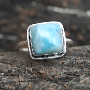 May include: A silver ring with a square blue and white gemstone.