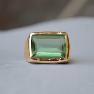 May include: A gold ring with a large, rectangular, light green gemstone.