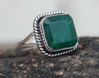 Puede incluir: Un anillo de plata con una gran piedra preciosa verde esmeralda engastada en un borde cuadrado con forma de cuerda.