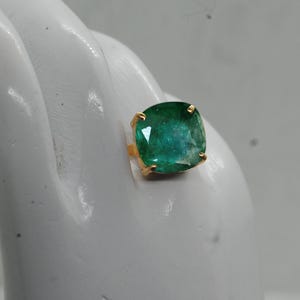 May include: A gold ring with a large, emerald green gemstone. The gemstone is a cushion cut and has a faceted finish.