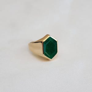 Puede incluir: Un anillo de oro con una gran piedra preciosa hexagonal de color verde oscuro.