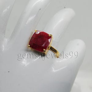 May include: A gold ring featuring a large, square-cut, deep red gemstone. The ring's band and setting are gold-colored. The image includes the text "gemsjewels99".