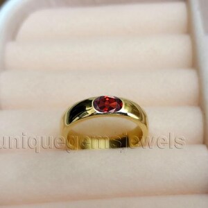 Könnte beinhalten: Ein Goldring mit einem einzigen roten Edelstein in der Mitte.