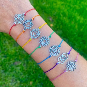 Puede incluir: Siete pulseras de cuerda de colores con dijes plateados que representan los siete símbolos de los chakras. Las pulseras están dispuestas en orden de arcoíris, comenzando con el rojo y terminando con el violeta.