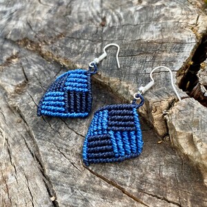 May include: A pair of blue and black macrame earrings with silver hooks. The earrings are in the shape of a diamond.