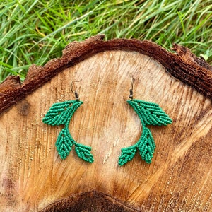 Könnte beinhalten: Ein Paar grüne, blattartige Ohrringe mit einem geknüpften Design. Die Ohrringe sind aus Schnur gefertigt und haben einen einfachen Hakenverschluss.