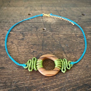 May include: A turquoise cord necklace with a wooden circle pendant. The pendant is wrapped with green cord and has a natural wood grain.