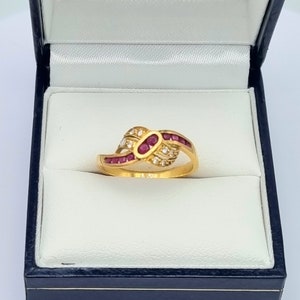 Könnte beinhalten: Ein goldener Ring mit einem Rubin- und Diamantendesign. Der Ring befindet sich in einer blauen Samt-Ringbox.