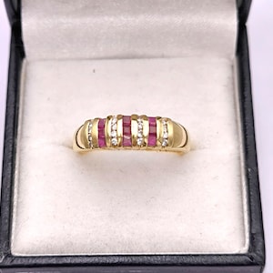 Puede incluir: Un anillo de banda de oro con una fila de piedras de rubí rosa y una fila de diamantes transparentes.