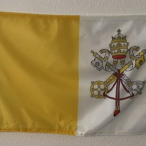 May include: A yellow and white flag with the coat of arms of Vatican City. The coat of arms features two crossed keys, a papal tiara, and a red tassel.