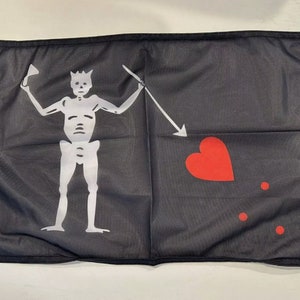 May include: Black flag featuring a white skeleton figure with a crown, holding a sword and a goblet. A red heart and three red dots are on the right side. The flag has a black border and grommets.