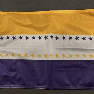 May include: A purple, white, and gold flag with a row of stars on each of the white stripes. The flag is made of a soft, woven fabric.