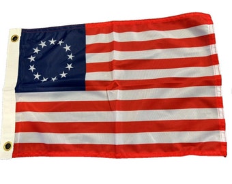 May include: A 13-star American flag with a blue field and 13 red and white stripes. The flag is made of fabric and has a white header with two brass grommets.