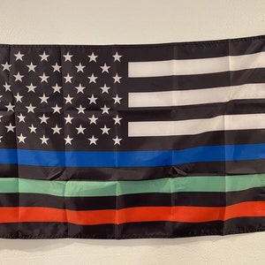 May include: A black flag with a thin blue line, a green line, and a red line. The flag also has white stripes and white stars on a blue field.