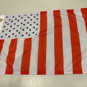 May include: American flag with red and white stripes and a blue canton with white stars. The flag has grommets on the left side for hanging. The flag is made of a lightweight material.