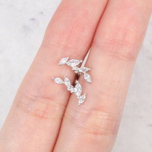 Puede incluir: Un pendiente de aro de plata con un delicado diseño de cristales transparentes en forma de marquesa dispuestos en forma de hoja.