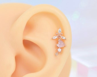 May include: A rose gold cartilage earring with a pink stone and clear crystal accents. The earring is in the shape of a flower with a delicate design.